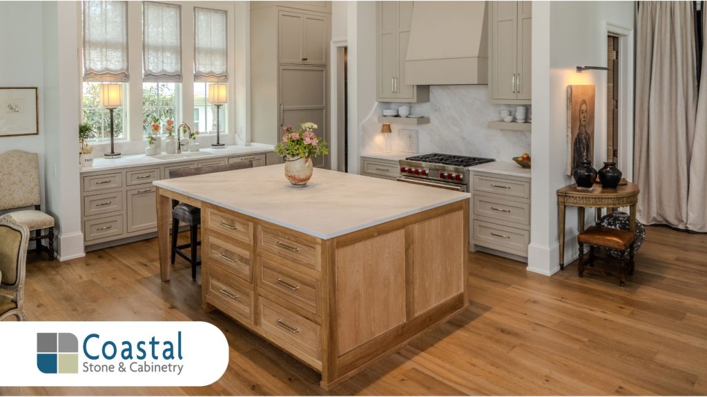 Coastal Stone and Cabinetry luxury kitchen installation with white perimeter cabinets a wood island base matching wood vent hood quartz countertops and glass pendant lights in Fairhope Alabama.
