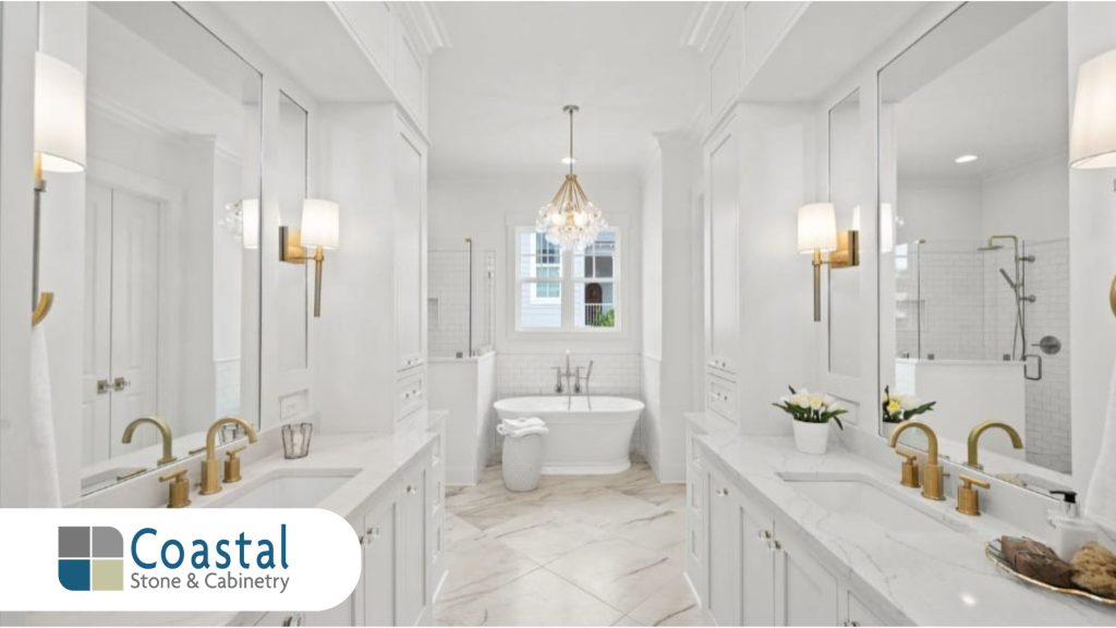Coastal Stone and Cabinetry luxury bathroom remodel featuring a freestanding soaking tub double white vanities with marble countertops gold faucets and a custom tile floor in Fairhope Alabama.