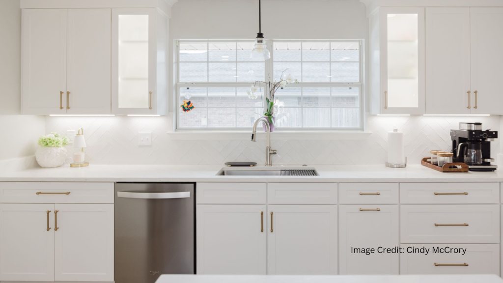 Coastal Stone and Cabinetry modern white kitchen featuring custom shaker cabinets gold hardware undermount sink herringbone backsplash and pristine quartz countertops in Fairhope Alabama.